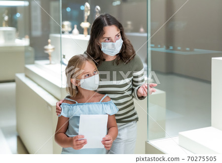 Woman visitor looking to art objects under glass with guide book 70275505