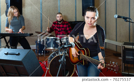 Attractive female soloist playing guitar and singing with her music band in sound studio 70275537