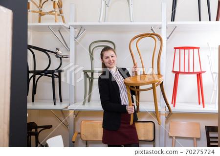 Saleswoman offering wooden chairs in store 70275724