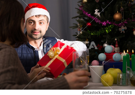Man in hat giving present to woman at New Year dinner 70275878