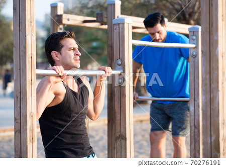 Smiling adult men are doing pull-ups 70276191