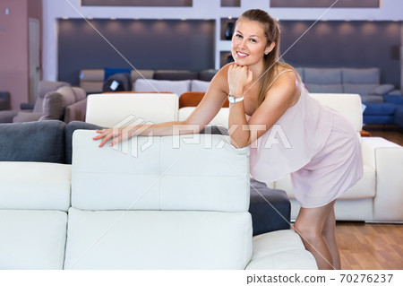 Female standing near sofa in the furniture store before the buying Female standing near sofa in the furniture store before the buying 70276237