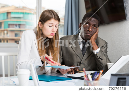 Unhappy managers working with laptop and documents at table in office Unhappy managers working with laptop and documents at table in office 70276256