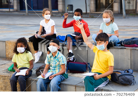 Preteen schoolchildren in protective masks with workbooks in schoolyard Preteen schoolchildren in protective masks with workbooks in schoolyard 70276409