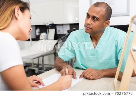 Male beautician filling medical card with woman client Male beautician filling medical card with woman client 70276773