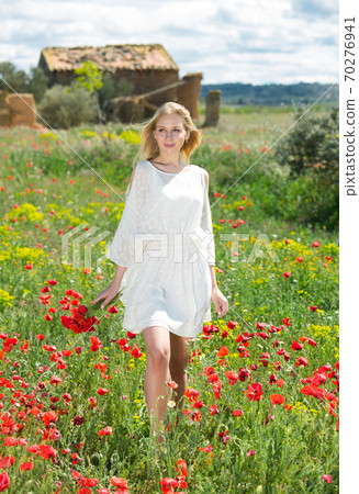 Woman in white dress walking and holding bouquet of poppies plants Woman in white dress walking and holding bouquet of poppies plants 70276941