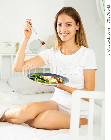 Cheerful young girl in lingerie having a salad while laying in the bed Cheerful young girl in lingerie having a salad while laying in the bed 70276943