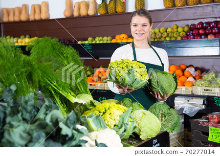 Young female seller in apron offering fresh greens and letuce Young female seller in apron offering fresh greens and letuce 70277014