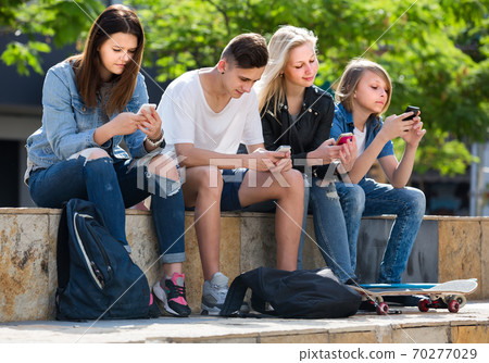 Portrait of four teenagers sitting with their mobile phones outdoors 70277029