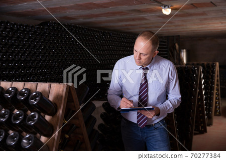 Wine producer with clipboard in wine cellar Wine producer with clipboard in wine cellar 70277384