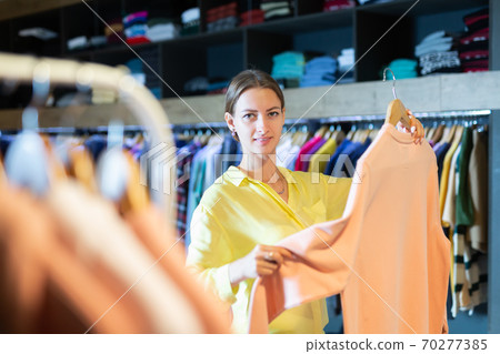 Portrait happy woman choosing new clothes on hangers Portrait happy woman choosing new clothes on hangers 70277385