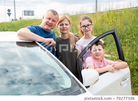 Family of four standing next to car 70277386