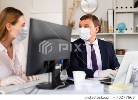 Manager in medical mask working with female colleague in office 70277668