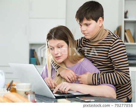 Young woman working at laptop with small son indoors Young woman working at laptop with small son indoors 70277858
