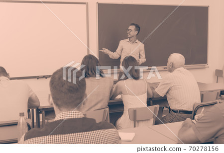 Adult lecturer talking to mixed age students 70278156