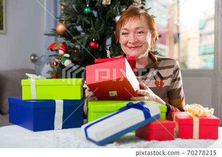 Happy elderly woman opens christmas gift boxes Happy elderly woman opens christmas gift boxes 70278215