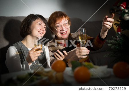 Happy mother and daughter drink champagne and watch TV on Christmas night Happy mother and daughter drink champagne and watch TV on Christmas night 70278229