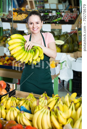 Portrait of smiling saleswoman with cluster of yellow bananas in store 70278679