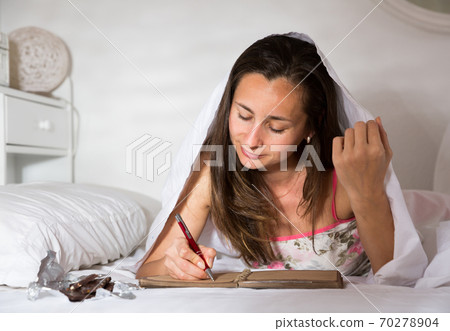 Woman elaxing under blanket and making schedule for tomorrow Woman elaxing under blanket and making schedule for tomorrow 70278904