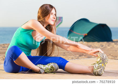 Woman in blue T-shirt is practicing stretching on the beach. Woman in blue T-shirt is practicing stretching on the beach. 70278910