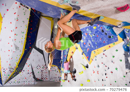Young sporty woman training at bouldering gym without special climbing equipment Young sporty woman training at bouldering gym without special climbing equipment 70279476