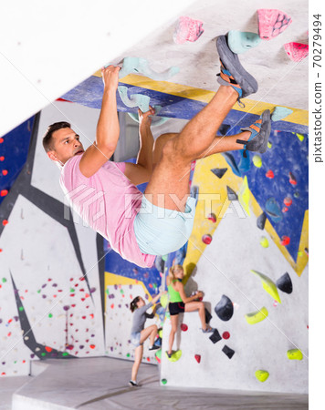 Male alpinist practicing indoor rock-climbing on artificial boulder without safety belts Male alpinist practicing indoor rock-climbing on artificial boulder without safety belts 70279494
