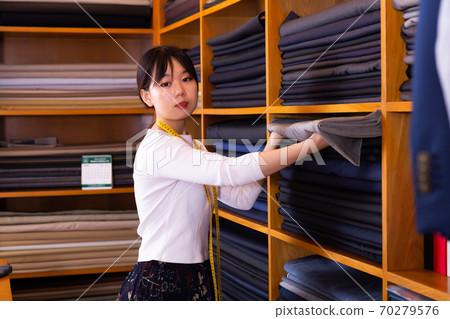 Saleswoman offering cloth in textile shop Saleswoman offering cloth in textile shop 70279576