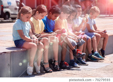 Positive children with mobile devices sitting at urban street Positive children with mobile devices sitting at urban street 70279593