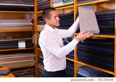 Male seller demonstrates various fabrics in store 70279594