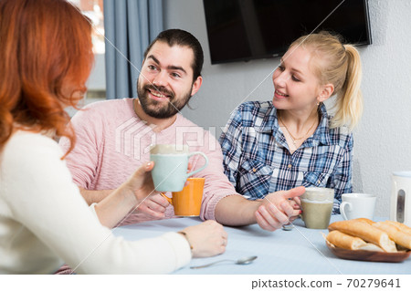 Smiling woman with cup of tea talking with adult children Smiling woman with cup of tea talking with adult children 70279641