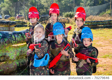 Friendly group of children paintball players in camouflage posing with guns on paintball playing field outdoors 70279646
