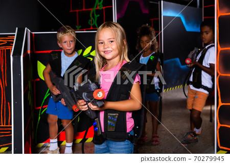 Smiling girl aiming laser gun at other players during lasertag game in dark room Smiling girl aiming laser gun at other players during lasertag game in dark room 70279945