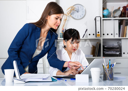 Businesswomen discussing over laptop at desk Businesswomen discussing over laptop at desk 70280024
