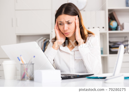 Tired young girl manager with laptop and documents working at office Tired young girl manager with laptop and documents working at office 70280275