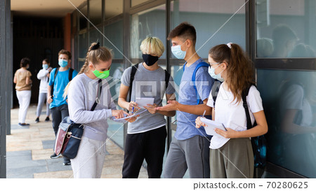 Group of students in protective masks discuss past lessons at a college on street Group of students in protective masks discuss past lessons at a college on street 70280625