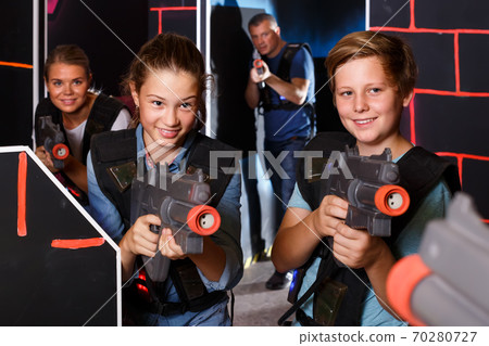 cheerful teen brother and sister with laser pistols playing laser tag with their parents cheerful teen brother and sister with laser pistols playing laser tag with their parents 70280727