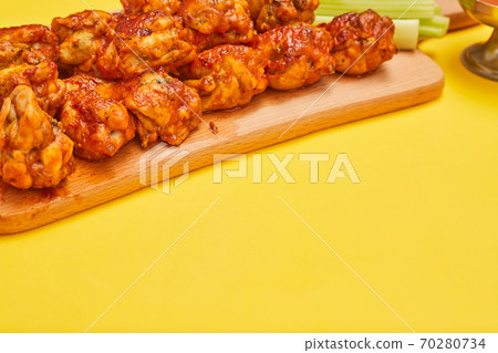 Buffalo chicken wings on a wooden board with celery on a yellow background, copy space 70280734