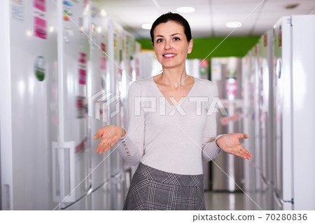 Positive woman choosing refrigerator in store of kitchen appliances 70280836