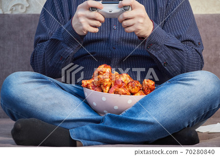 man playing on the couch with a plate of Buffalo Chicken Wings, copy space 70280840