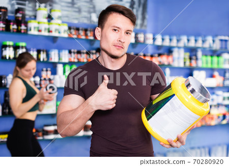 Confident athletic guy posing in shop of sports nutritional supplements, giving thumbs up 70280920