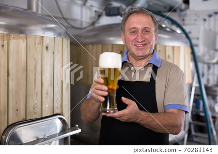 Portrait of brewer who is standing with glass of beer on his workplace 70281143