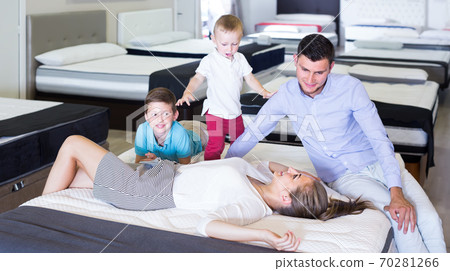 Young woman with husband and sons lying on back on tested mattress in store Young woman with husband and sons lying on back on tested mattress in store 70281266