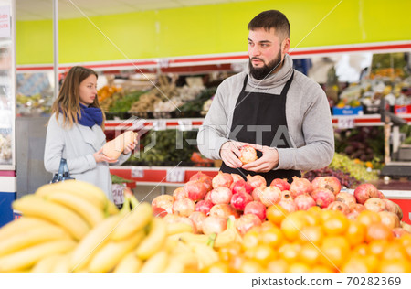 Supermarket employee will lay out ripe pomegranates on the counter Supermarket employee will lay out ripe pomegranates on the counter 70282369