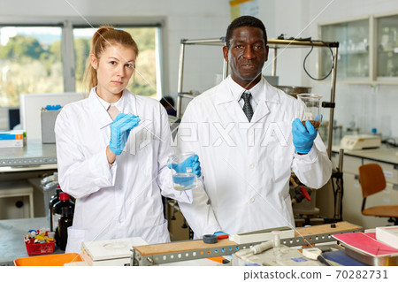 Focused lab technicians in gloves working with reagents and test tubes Focused lab technicians in gloves working with reagents and test tubes 70282731