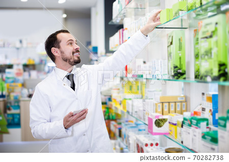 Smiling man pharmacist looking rows of drugs Smiling man pharmacist looking rows of drugs 70282738