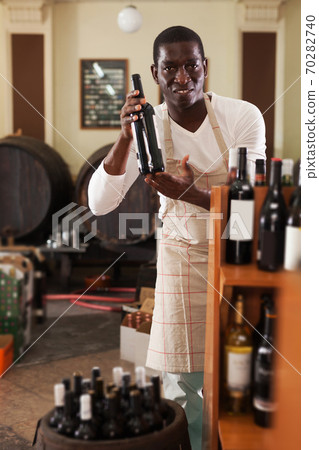 afro male seller of wine shop offering wine bottle to buy afro male seller of wine shop offering wine bottle to buy 70282740