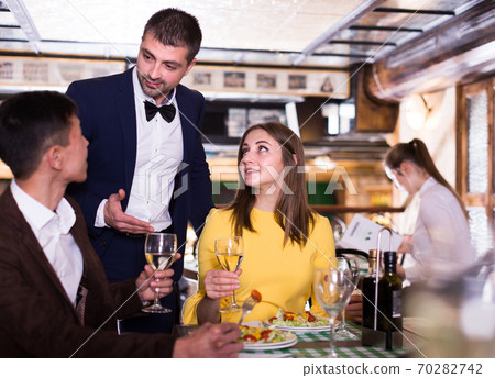 Male administrator is asking about service from smiling couple who is drinking wine in restaurant. Male administrator is asking about service from smiling couple who is drinking wine in restaurant. 70282742