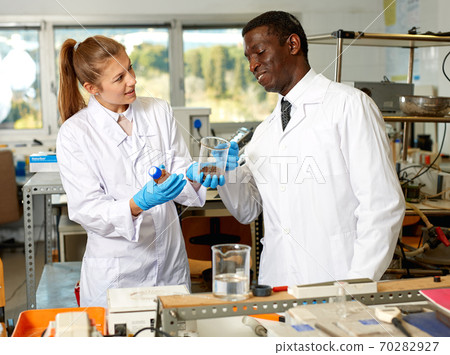 Focused lab technicians in gloves working with reagents and test tubes Focused lab technicians in gloves working with reagents and test tubes 70282927