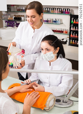 friendly nail technician offering to female client to choose color of nail polish in beauty salon friendly nail technician offering to female client to choose color of nail polish in beauty salon 70282931