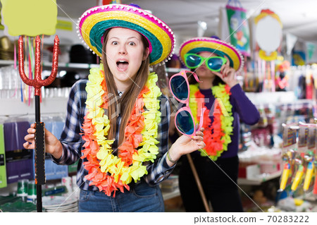 Comically dressed positive girl joking while visiting festive accessories shop Comically dressed positive girl joking while visiting festive accessories shop 70283222